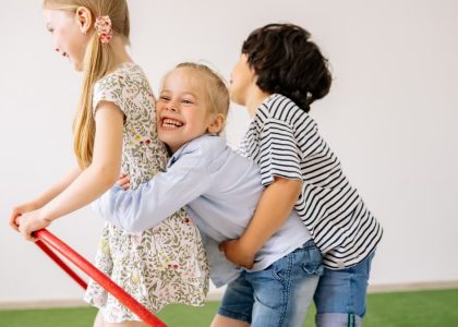 Three children joyfully play indoors with a hula hoop, showcasing happiness and togetherness.
